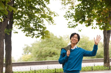 Açık havada duran, sallayarak kendinden emin gülümseyen Asya iş adamı