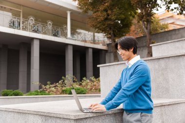 Açık havada dizüstü bilgisayar kullanan gülümseyen Asya iş adamı
