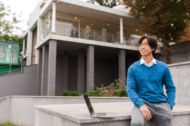 Açık havada dizüstü bilgisayar kullanan gülümseyen Asya iş adamı