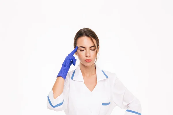 疲れ若い女性医師の白い背景に分離立って制服やゴム手袋を着用 — ストック写真