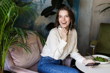 Kapalı kafede otururken çok güzel genç kadının fotoğrafını cep telefonu ile konuşurken salata yemek.