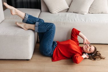 Neşeli genç raslantı giyimli bir yere vasıl ev, döşeme kadın kulaklık ile müzik dinlemek