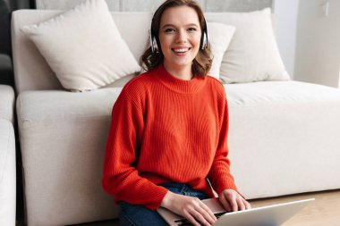 Mutlu genç raslantı giyimli bir katta evde oturan kadın dizüstü bilgisayar ile eğitim