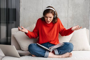 Yorgun genç raslantı giyimli evde, bir kanepede oturan kadın dizüstü bilgisayar ile eğitim