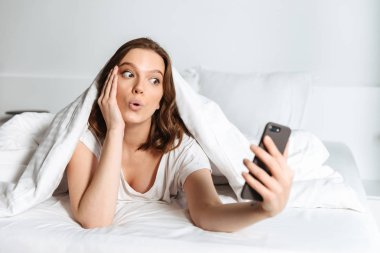Bir selfie alarak evde, battaniyenin altında yatakta yalan çekici gülümseyen genç kadın