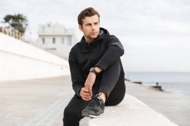 Yakışıklı sportif 30s erkekte seaside, tahta oturan siyah spor giyim görüntü