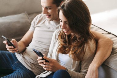 Cep telefonu kullaranarak bir kanepede evde oturan mutlu genç çift