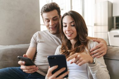 Cep telefonu kullaranarak bir kanepede evde oturan mutlu genç çift