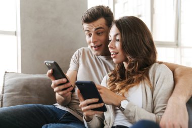 Cep telefonu kullaranarak bir kanepede evde oturan mutlu genç çift