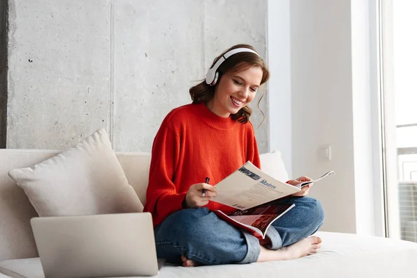 Neşeli Genç Rahat Bir Kanepede Evde Oturan Kulaklıklar Dizüstü Bilgisayar — Stok fotoğraf