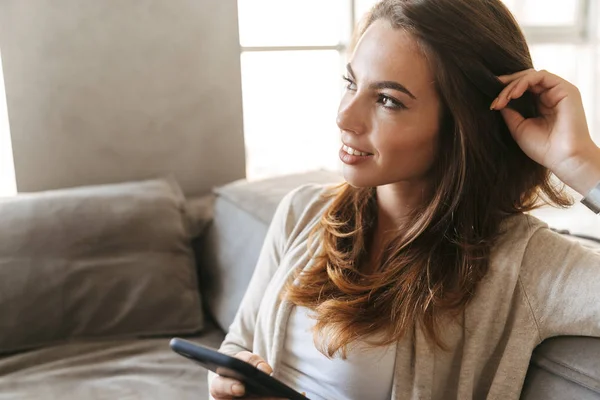 Giovane Donna Sorridente Che Tiene Telefono Cellulare Seduta Divano Casa — Foto Stock