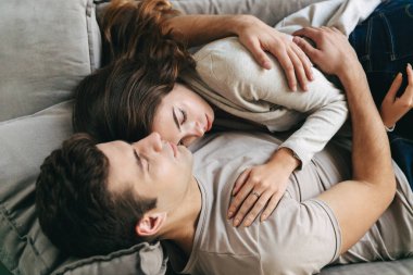 Mutlu genç çift evde, bir kanepede rahatlatıcı kucaklayan