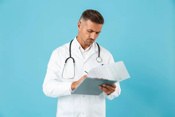 英俊的医生的画像与听诊器拿着健康卡片站立在蓝色背景隔离 — 图库照片