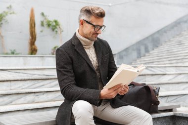 Yakışıklı adam açık havada otururken bir kitap okuma ceket