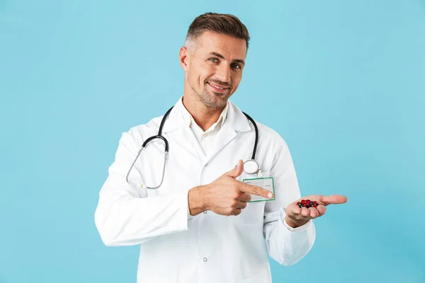 照片中 一个英俊的成熟的男人医生提出隔离在蓝色墙壁背景举行药丸维生素 — 图库照片