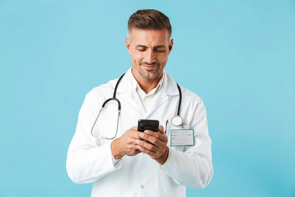 Fotky Hezký Lékař Nosí Bílý Plášť Stetoskop Držení Smartphone Stojící — Stock fotografie