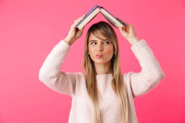 Kitap başını tutarak pembe arka plan üzerinde izole neşeli genç sarışın kız ayakta