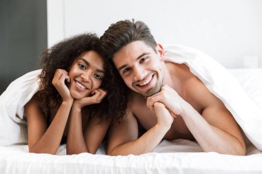 Güzel mutlu genç çok ırklı bir çift yatakta battaniyenin altında rahatlatıcı