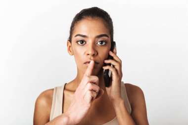 Afrikalı kadın tarafından cep telefonu birinin elini sessizlik jest gösterilen süre konuşmak beyaz duvar arka plan üzerinde izole poz görüntü.
