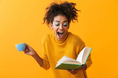 Gönüllülük a kitap, kahve içme sarı arka plan üzerinde izole kazak ayakta giyen karışık Afrika kadın