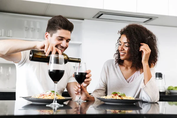 美しい若い民族カップル ロマンチックな夕食を家で 赤ワインを飲むと注ぐパスタを食べて — ストック写真