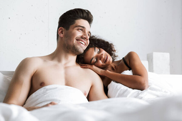 Красивая счастливая молодая многонациональная пара отдыхает в постели под одеялом
