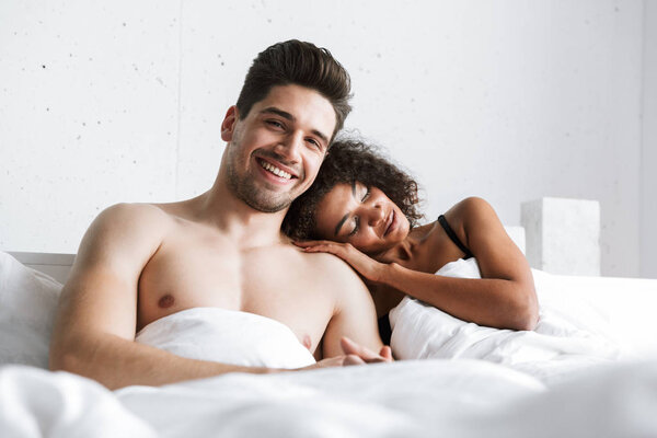 Красивая счастливая молодая многонациональная пара отдыхает в постели под одеялом

