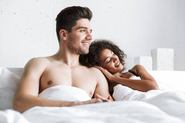 Красивая счастливая молодая многонациональная пара отдыхает в постели под одеялом
