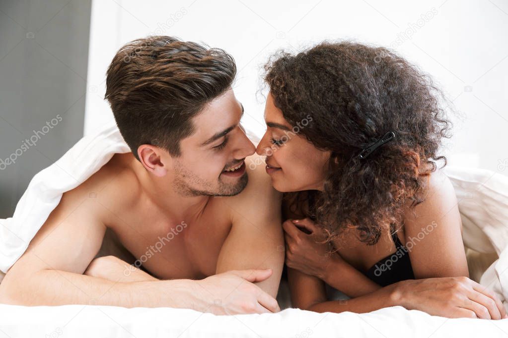Beautiful happy young multiethnic couple relaxing in bed under blanket