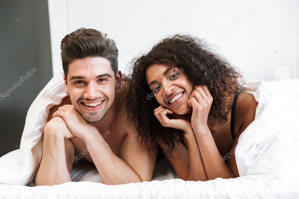 Beautiful happy young multiethnic couple relaxing in bed under blanket