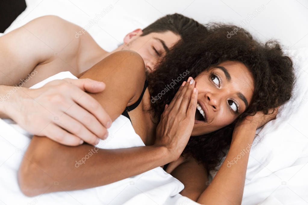 Beautiful happy young multiethnic couple relaxing in bed under blanket, excited woman