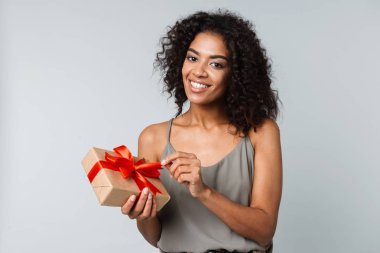 Mutlu genç Afrikalı kadın kayıtsızca giyinmiş gri arka plan üzerinde izole ayakta tutan bir hediye kutusu
