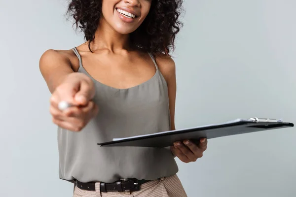 幸せな若いアフリカ女性のカジュアル服装分離灰色の背景の上に立って保持メモ帳 ペンで指している画像をトリミング — ストック写真