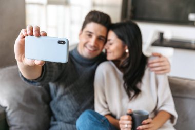 Evde bir kanepede oturan, çay içme, bir selfie alarak mutlu genç çift