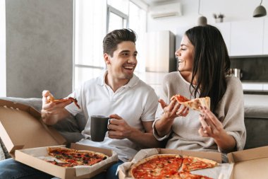 Evde bir kanepede oturan, pizza yemek, Tv izlerken neşeli genç çift