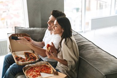 Evde bir kanepede oturan, pizza yemek, Tv izlerken neşeli genç çift