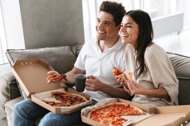 Evde bir kanepede oturan, pizza yemek, Tv izlerken neşeli genç çift