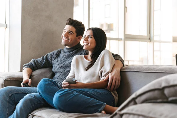 Pareja Joven Feliz Sentada Sofá Casa Viendo Televisión Tomando —  Fotos de Stock