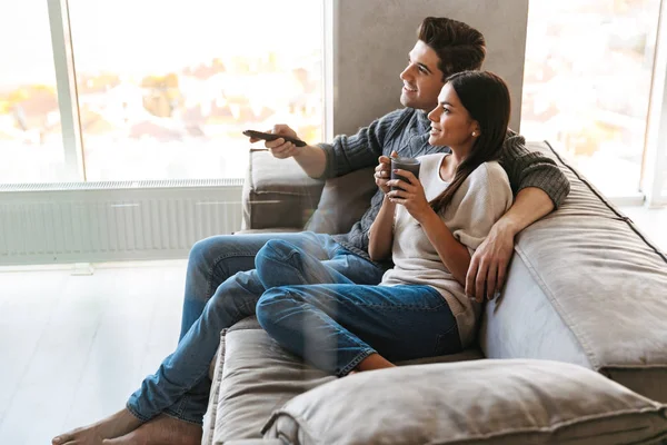幸せな若いカップル 自宅でソファに座って テレビを見て お茶を飲む — ストック写真