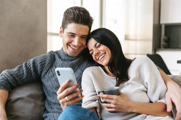 幸福的年轻夫妇坐在家里的沙发上 看着手机 — 图库照片