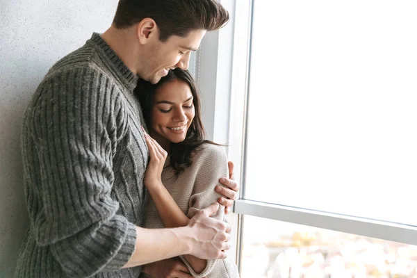 Feliz Pareja Joven Encantadora Pie Junto Ventana Casa Abrazando —  Fotos de Stock