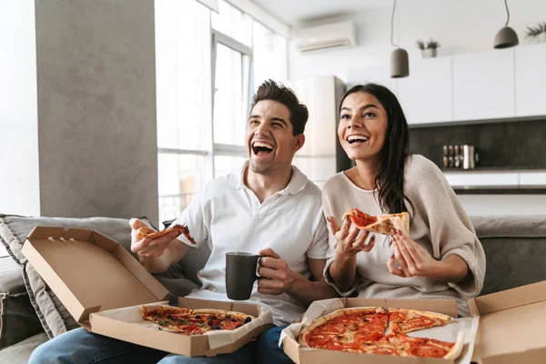 Wesoły Młoda Para Siedzi Kanapie Domu Jedzenie Pizzy Oglądanie Telewizji — Zdjęcie stockowe