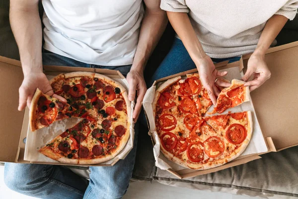 Top view of a couple eating two big pizzas on a couch
