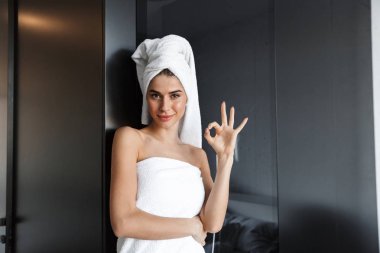 Beautiful young woman wrapped in bath towel standing at the bedroom clipart