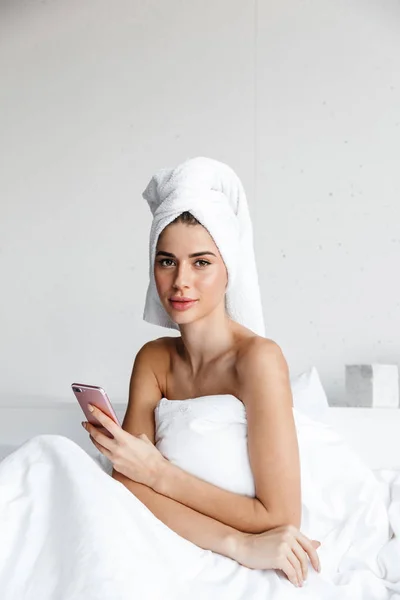 Cep Telefonu Tutan Güzel Genç Kadın Yatakta Oturmuş Banyo Havlusu — Stok fotoğraf