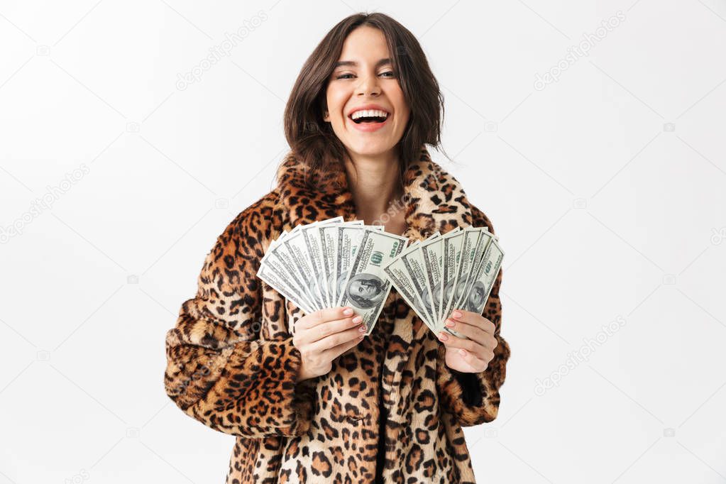 Beautiful woman wearing leopard fur coat standing isolated over white, showing money banknotes