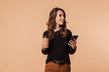 Görüntü güzel kadın 20'li yaşlarda holding cep telefonu ve paket kahve bej renkli arka plan üzerinde izole