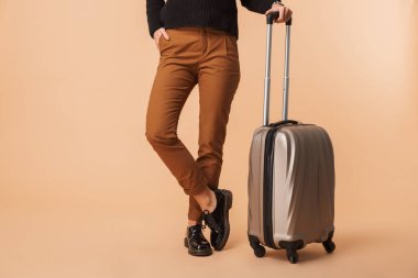 Bej renkli arka plan üzerinde izole bir seyahat çantası ile duran genç bir kadın resim kırpılmış