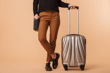 Bej renkli arka plan üzerinde izole bir seyahat çantası ile duran genç bir kadın resim kırpılmış