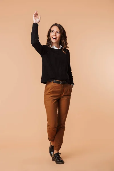 陽気な若い女性の身に着けているセーター立っているベージュの背景の上分離された離れて見て完全な長さ — ストック写真